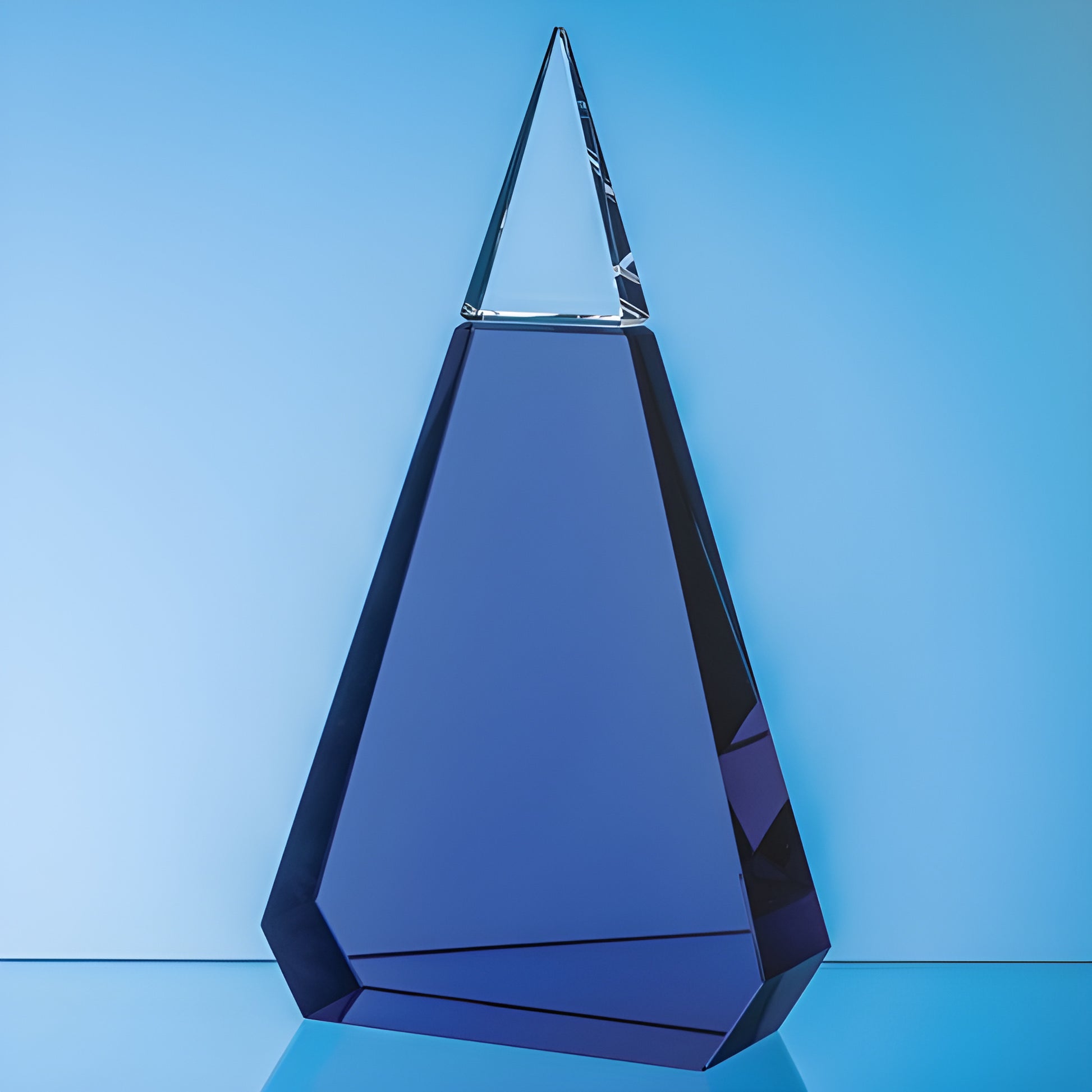 Cobalt blue and clear optical crystal prism award with geometric design on blue background.