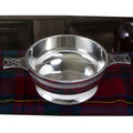 Pewter quaich bowl with Celtic knot handles on Scottish tartan cloth.
