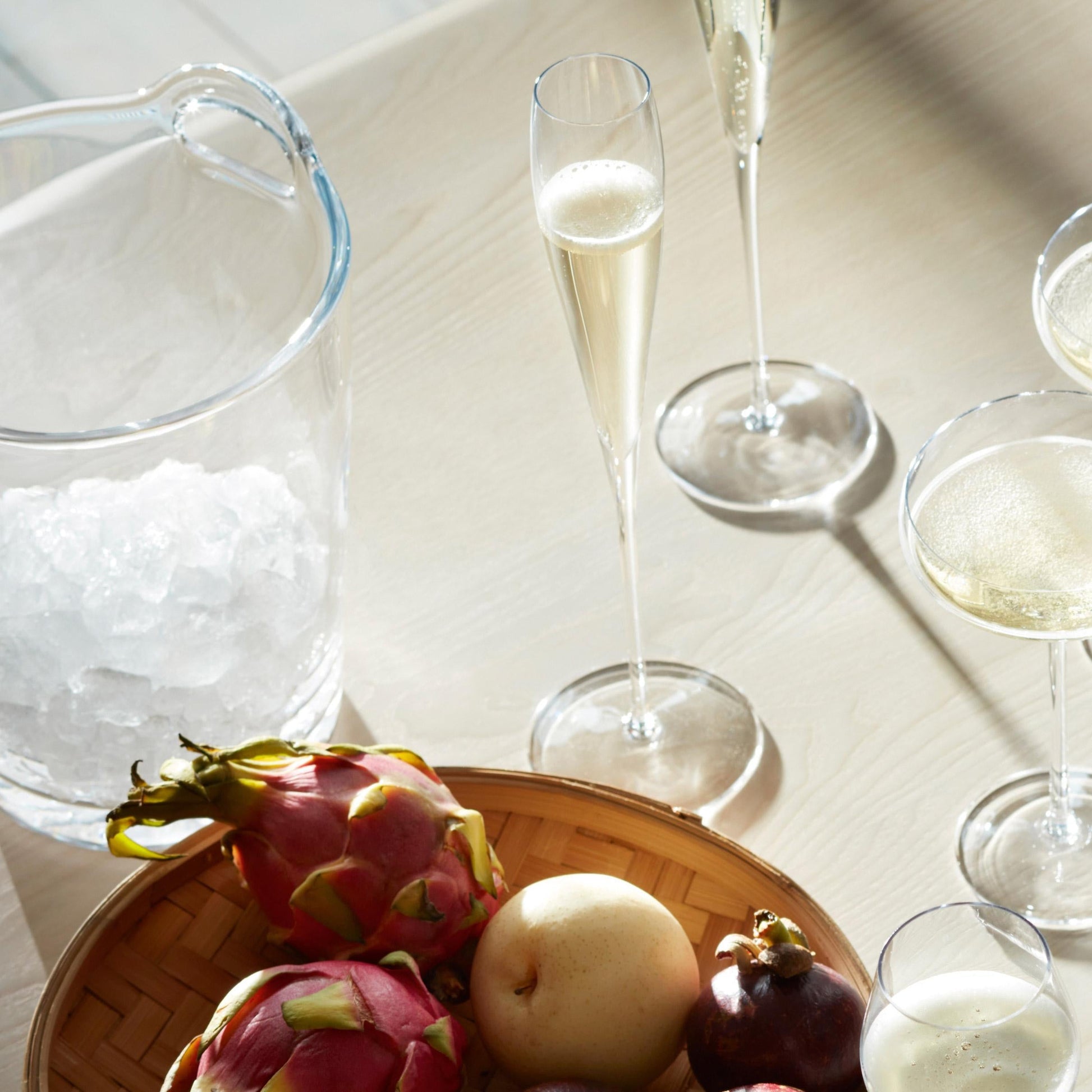 Champagne flutes and coupe glasses with fruit platter by an ice bucket on a bar table.
