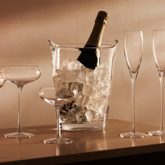 Champagne bottle in ice bucket with empty glasses on elegant dining table.
