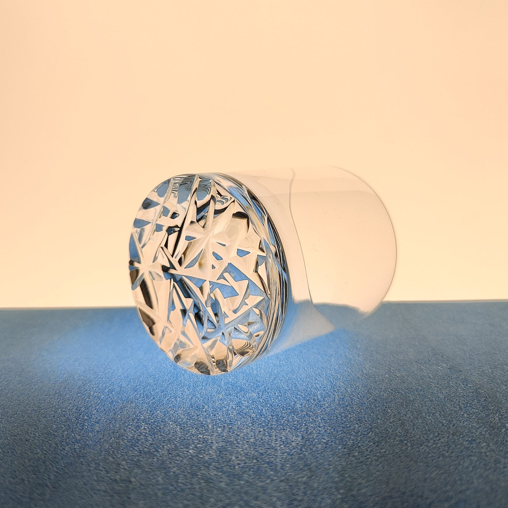 Crystal tumbler lying on its side with engraved bottom, casting light and shadow.