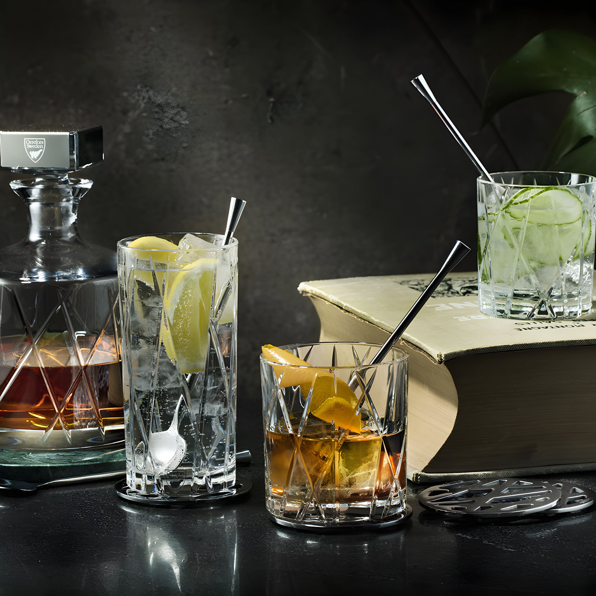 Elegant glass decanter and mixed drinks in textured glasses on a dark countertop with a book in the background.