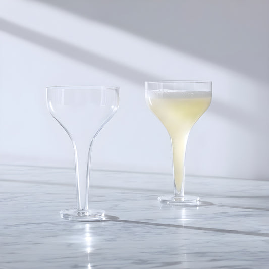Two Epoque cocktail saucer glasses, one empty and one filled, on a marble surface
