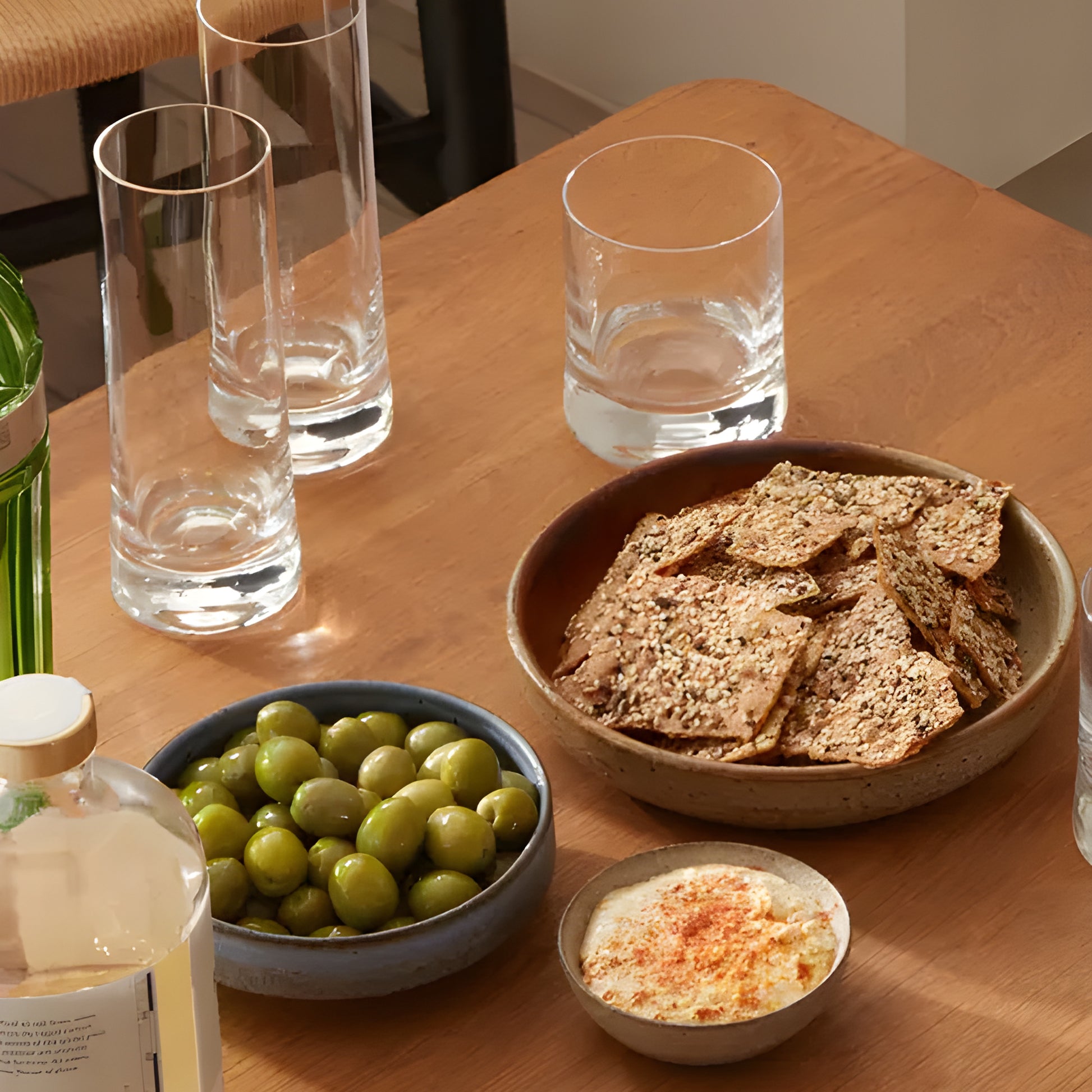 Gin highball glasses on a table with olives, hummus, and crackers.