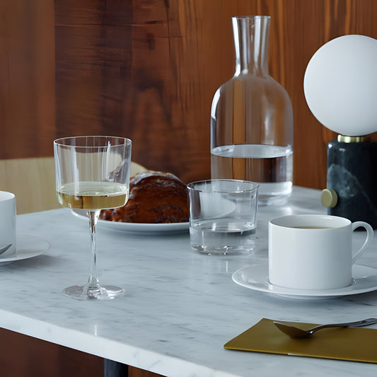 Modern dining table with wine glass, marble top, and water carafe.