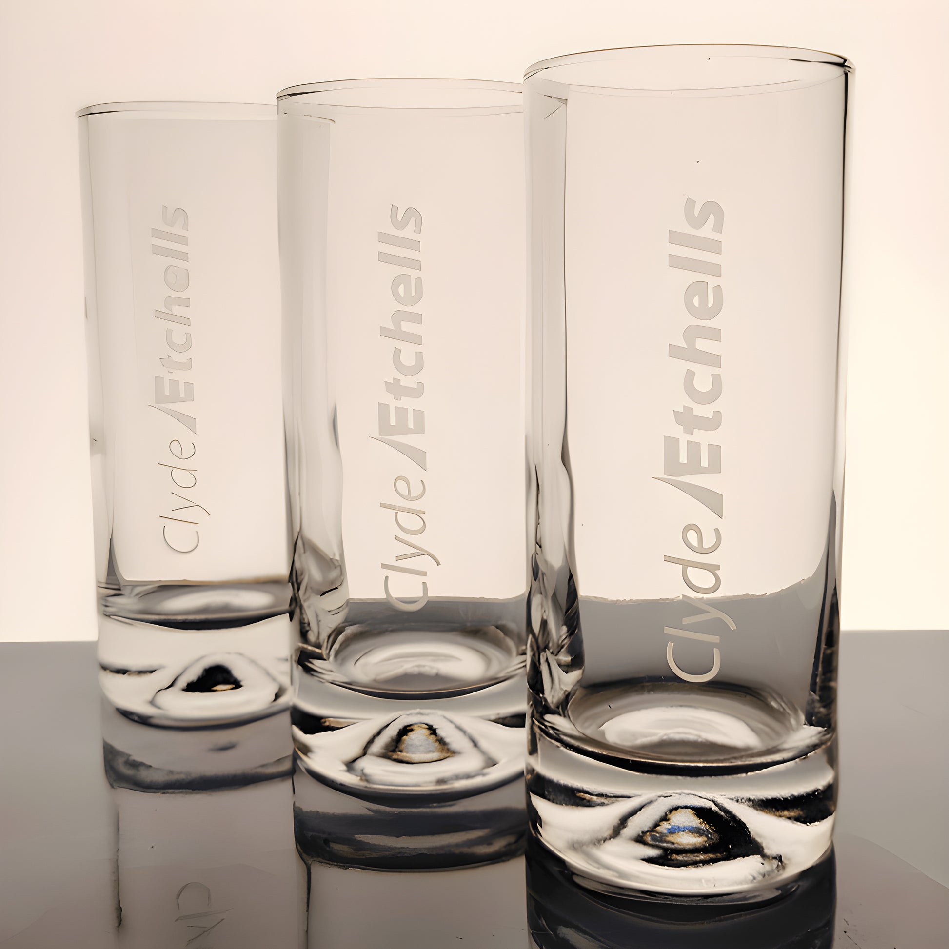 Set of three tall clear glasses with etched logo against a light background.