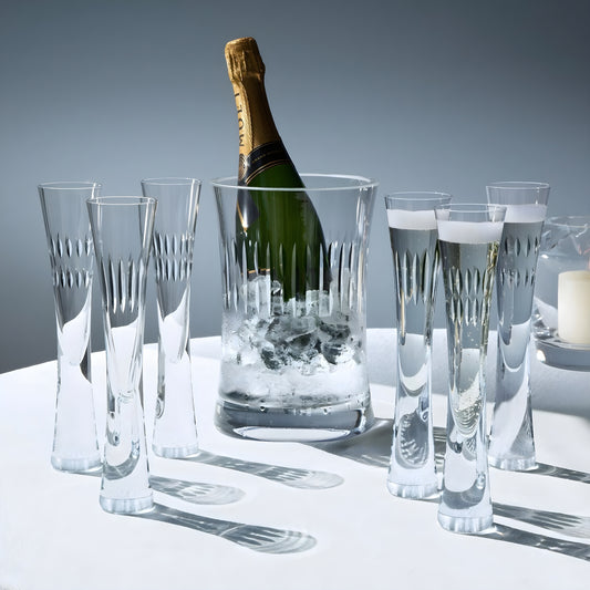 Crystal champagne flutes and ice bucket with bottle on white table.