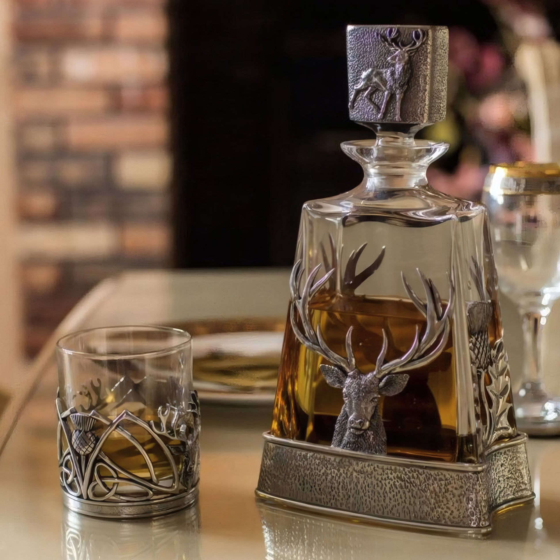 Decorative whisky decanter with stag and thistle design next to matching glass on table.