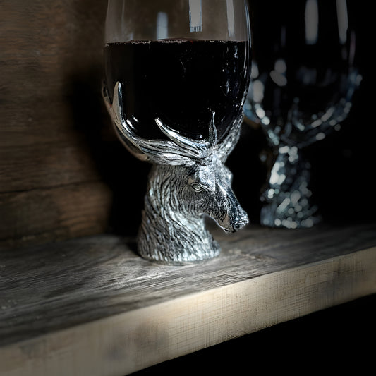 Decorative stag head wine glasses with silver antlers on wooden shelf.