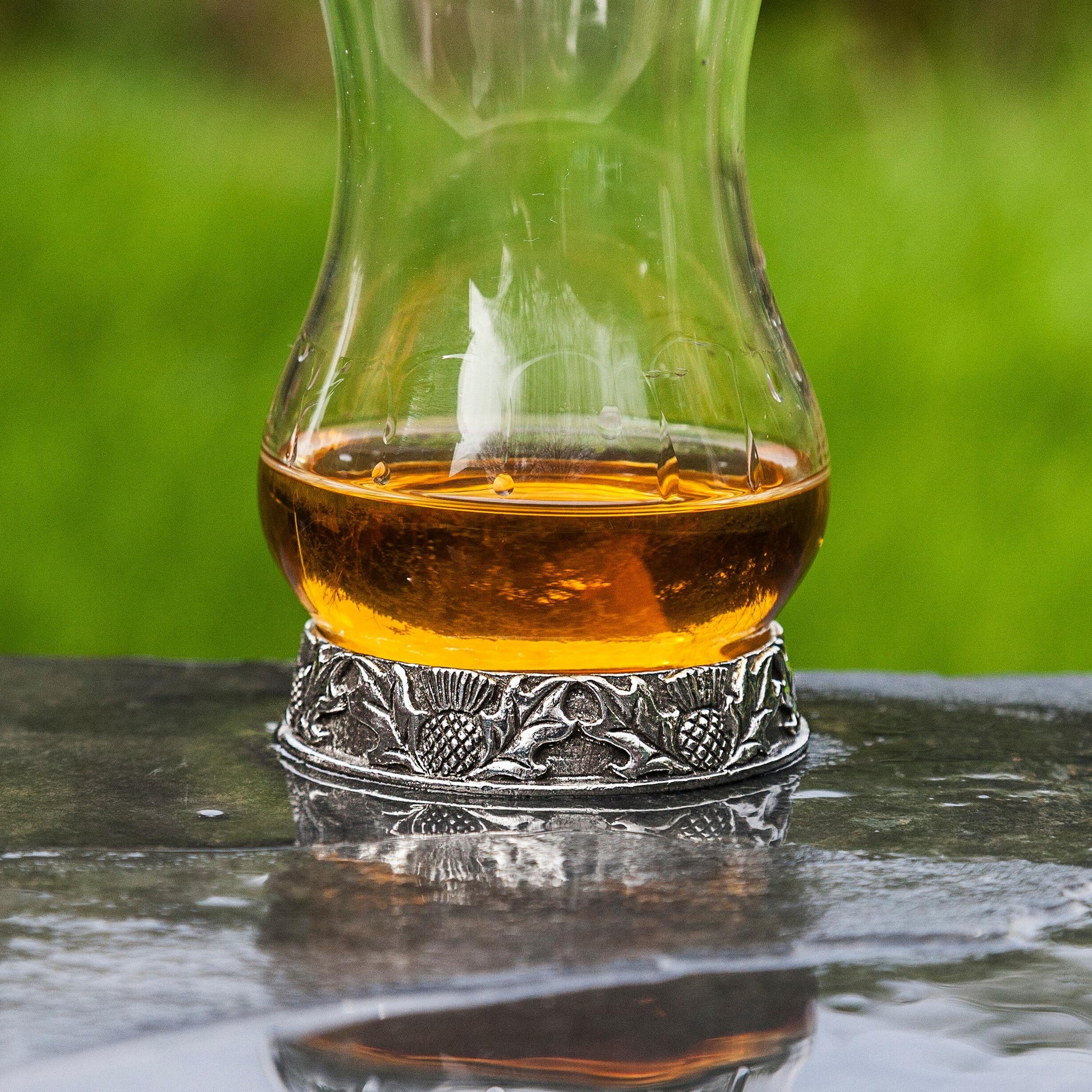 Whisky glass with single malt on decorative metal base outdoors.