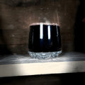 Thistle tumbler glass filled with burgundy wine on a wooden shelf.