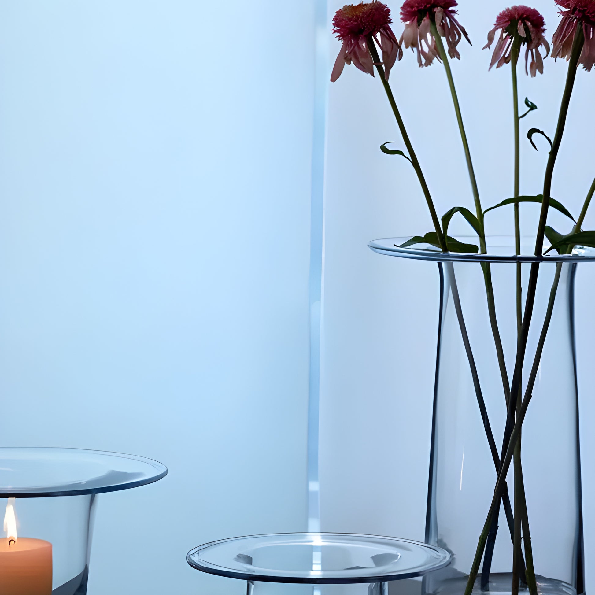 Glass vases with pink flowers and a lit candle on a table.
