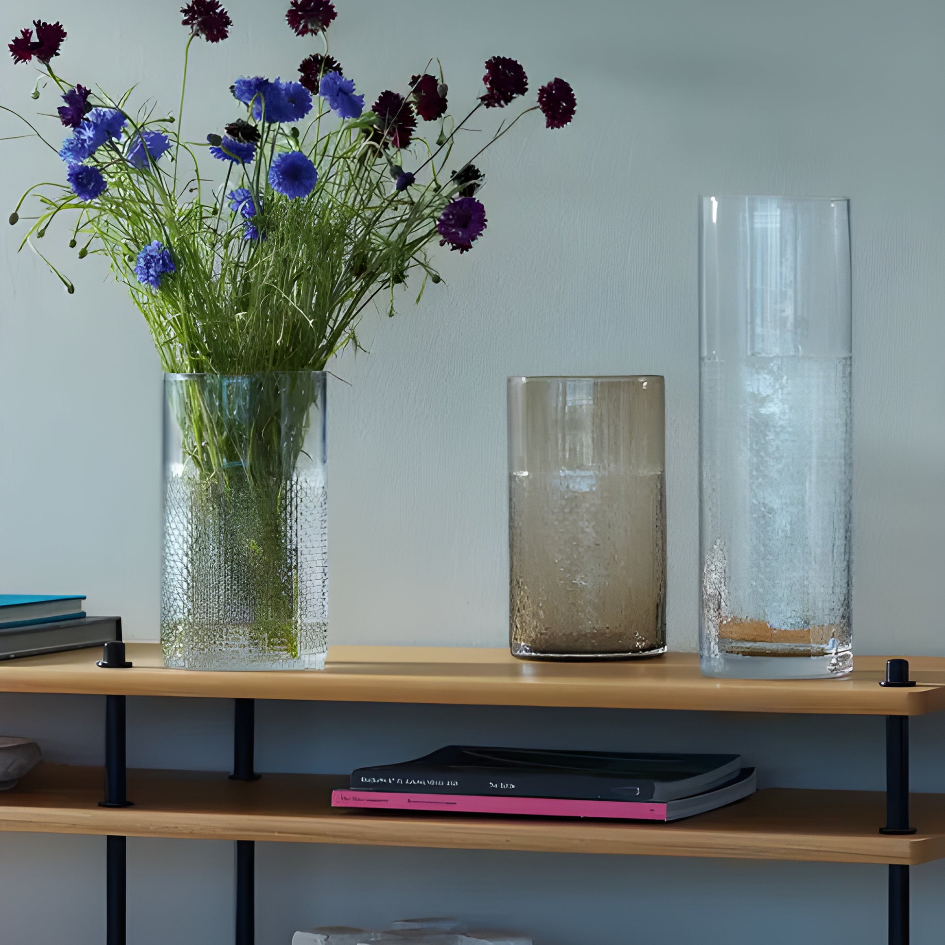 Modern glass vases with flowers on a minimalist bookshelf.