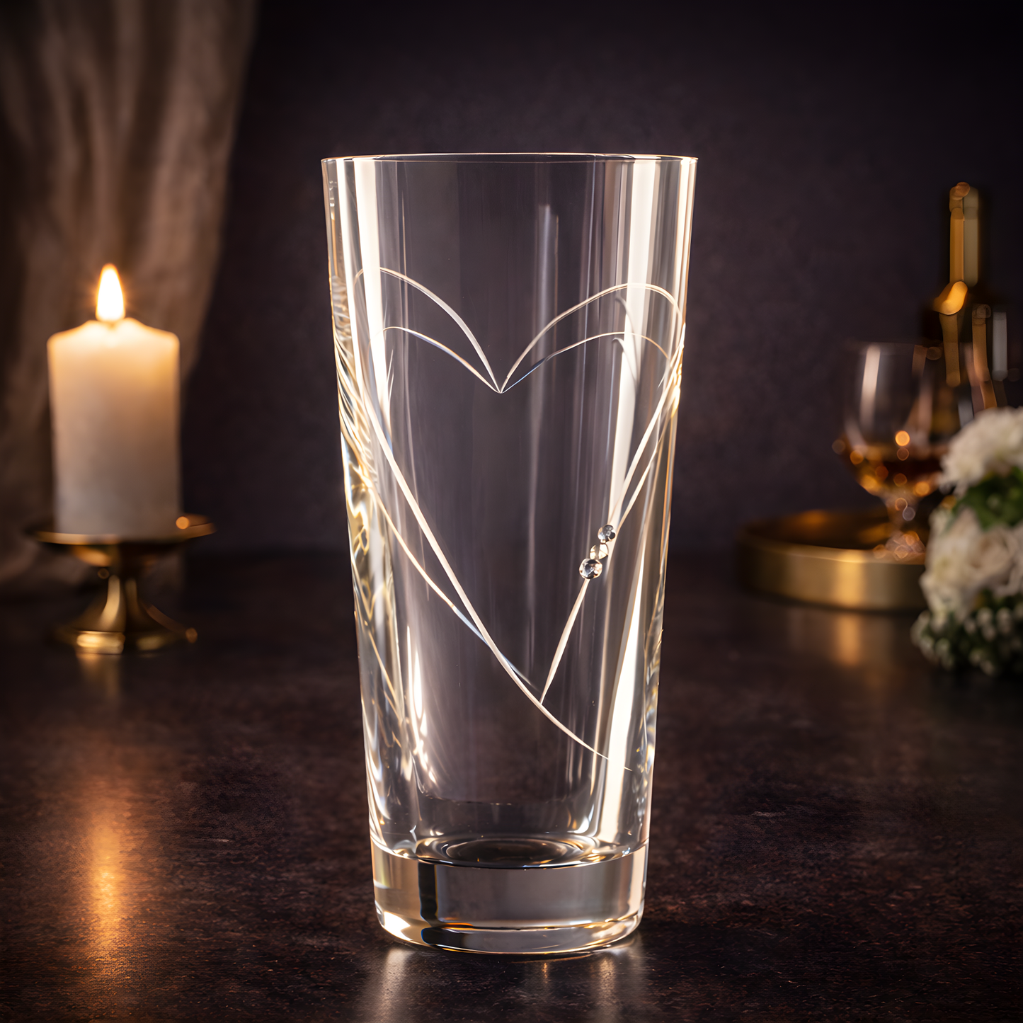 Crystal vase with heart design near lit candle and flowers.