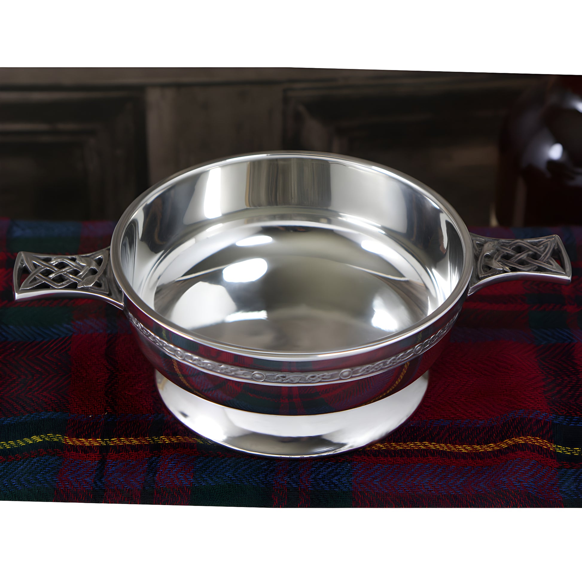 Pewter quaich bowl with Celtic knot handles on Scottish tartan cloth.
