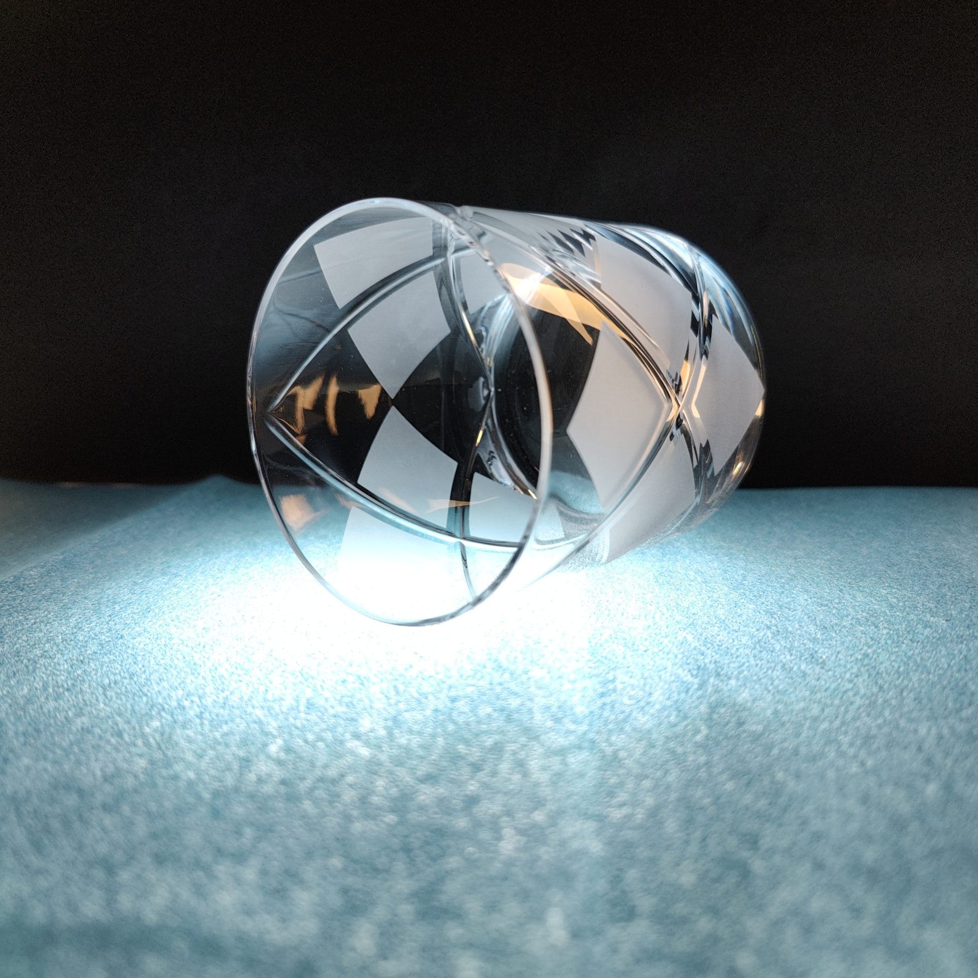 Crystal tumbler with argyle pattern on illuminated surface against dark background.