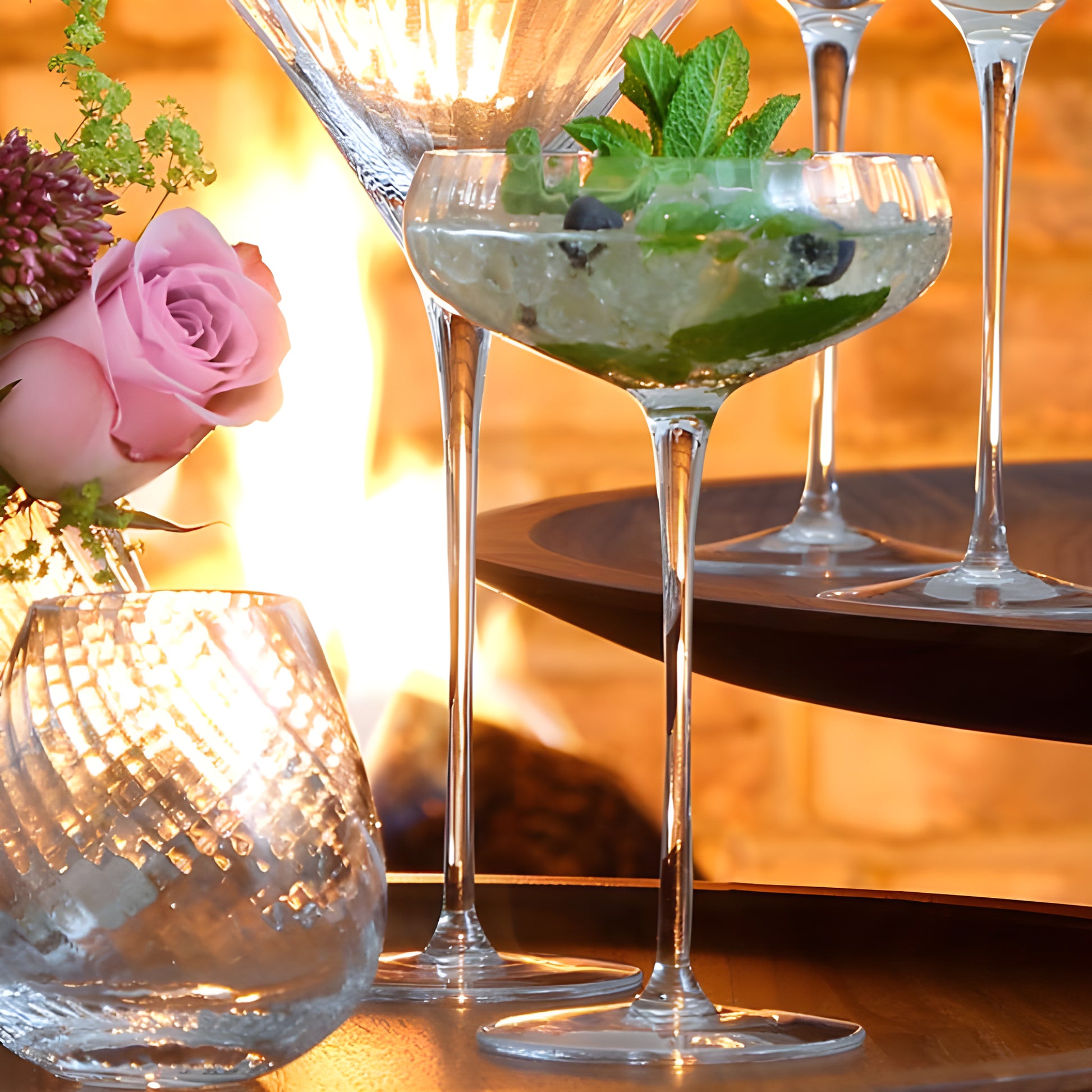 Aurelia champagne saucer with mojito cocktail beside a pink rose and candles.