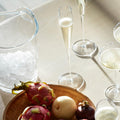Champagne flutes and coupe glasses with fruit platter by an ice bucket on a bar table.