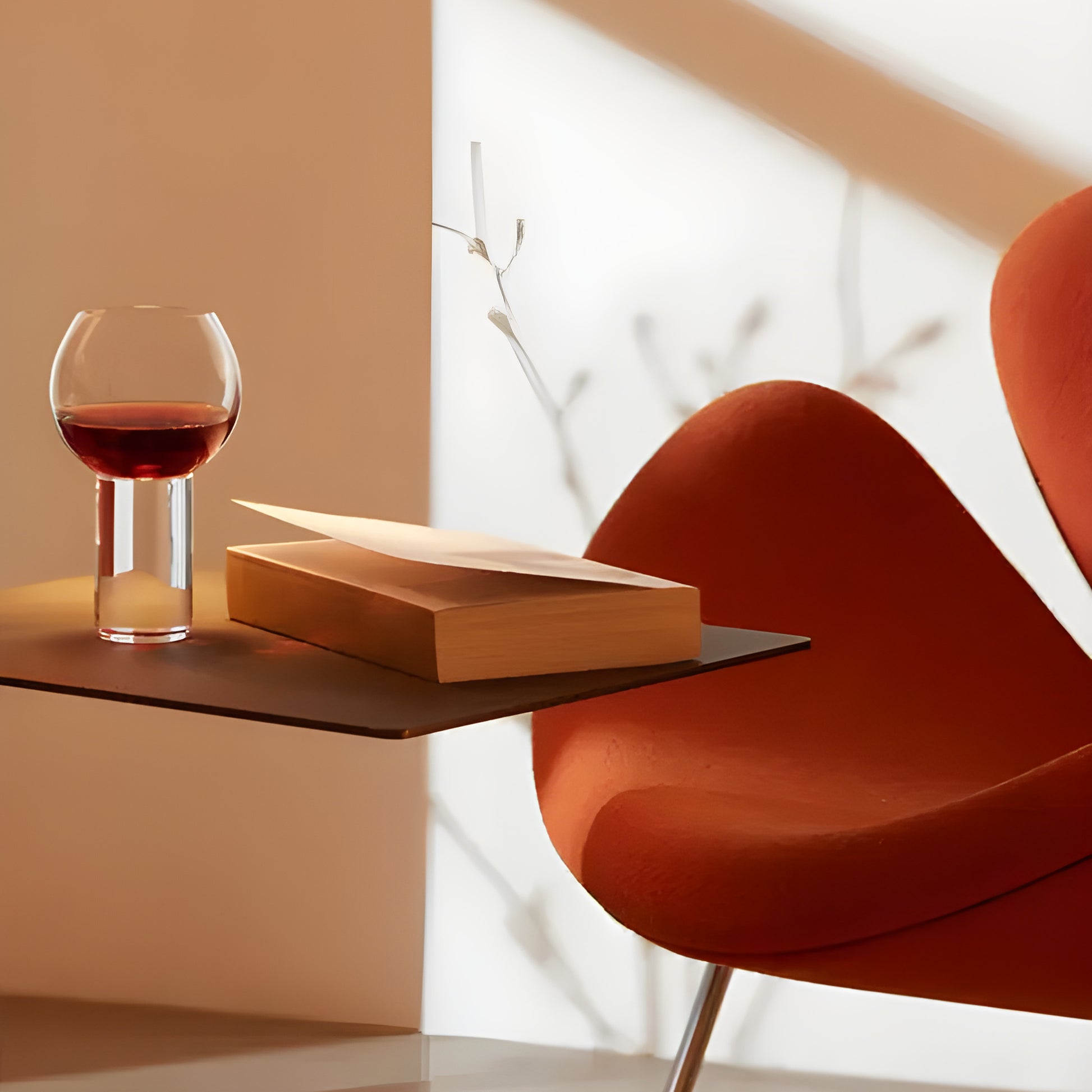 Modern glass of red wine next to book on a table with a mid-century chair.