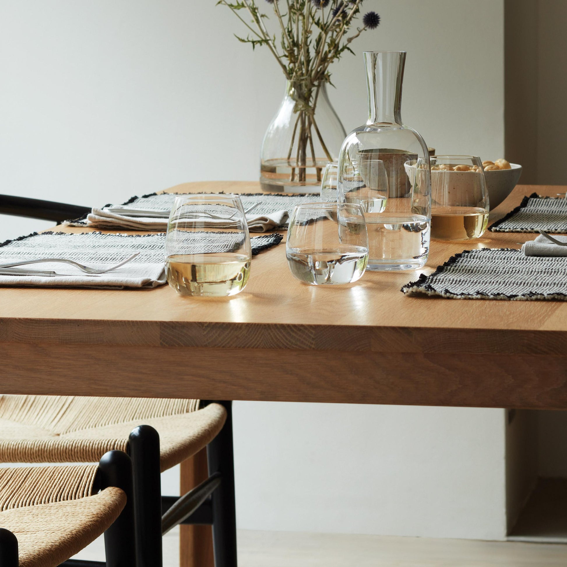 Modern dining setup with stemless glasses on a wooden table and purple flowers in a vase.