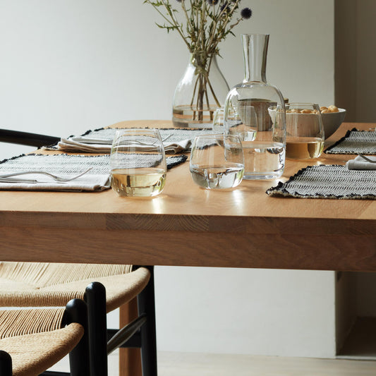 Modern dining setup with stemless glasses on a wooden table and purple flowers in a vase.
