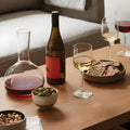 Wine and snacks arranged on a wooden coffee table with glasses and a decanter.