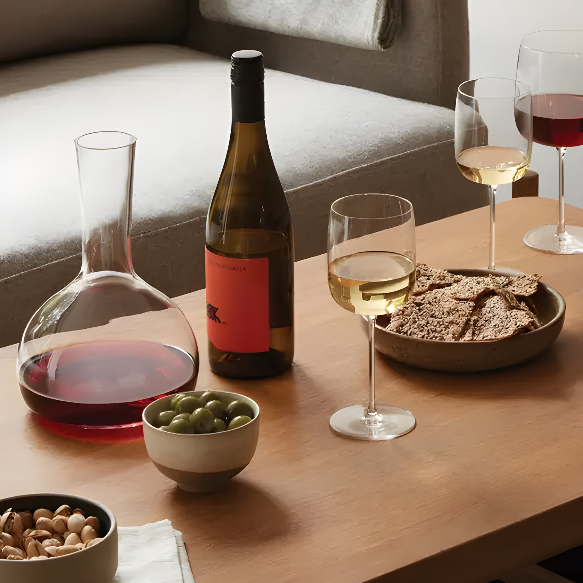 Wine and snacks arranged on a wooden coffee table with glasses and a decanter.