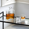 Cask decanter set with two whiskey glasses on a glass bar cart.