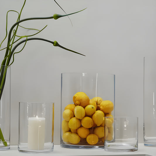 Glass vase with lemons next to a candle holder on a shelf.