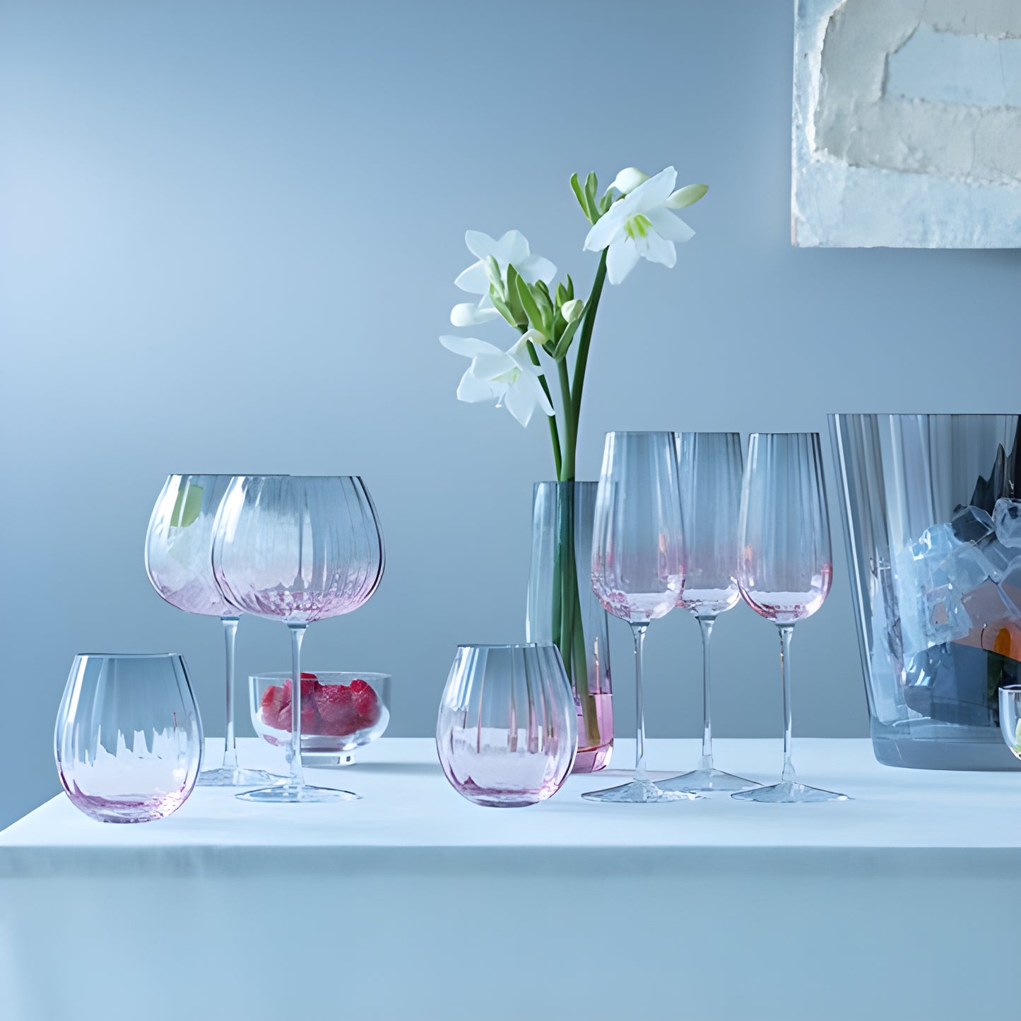 Pink glassware and champagne flute on table with white flowers and ice bucket.