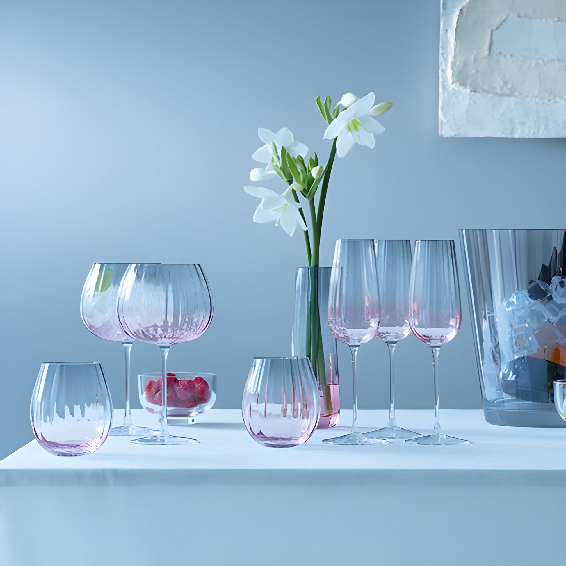 Pink glassware and champagne flute on table with white flowers and ice bucket.