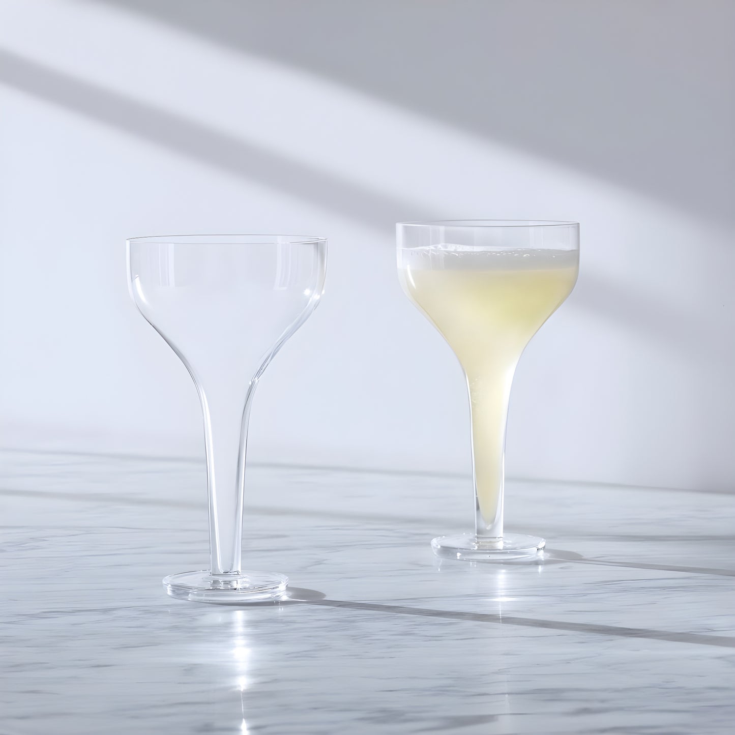 Two Epoque cocktail saucer glasses, one empty and one filled, on a marble surface