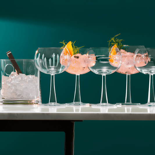 Four gin and tonic glasses filled with ice and garnishes on a white table, with a green wall background.