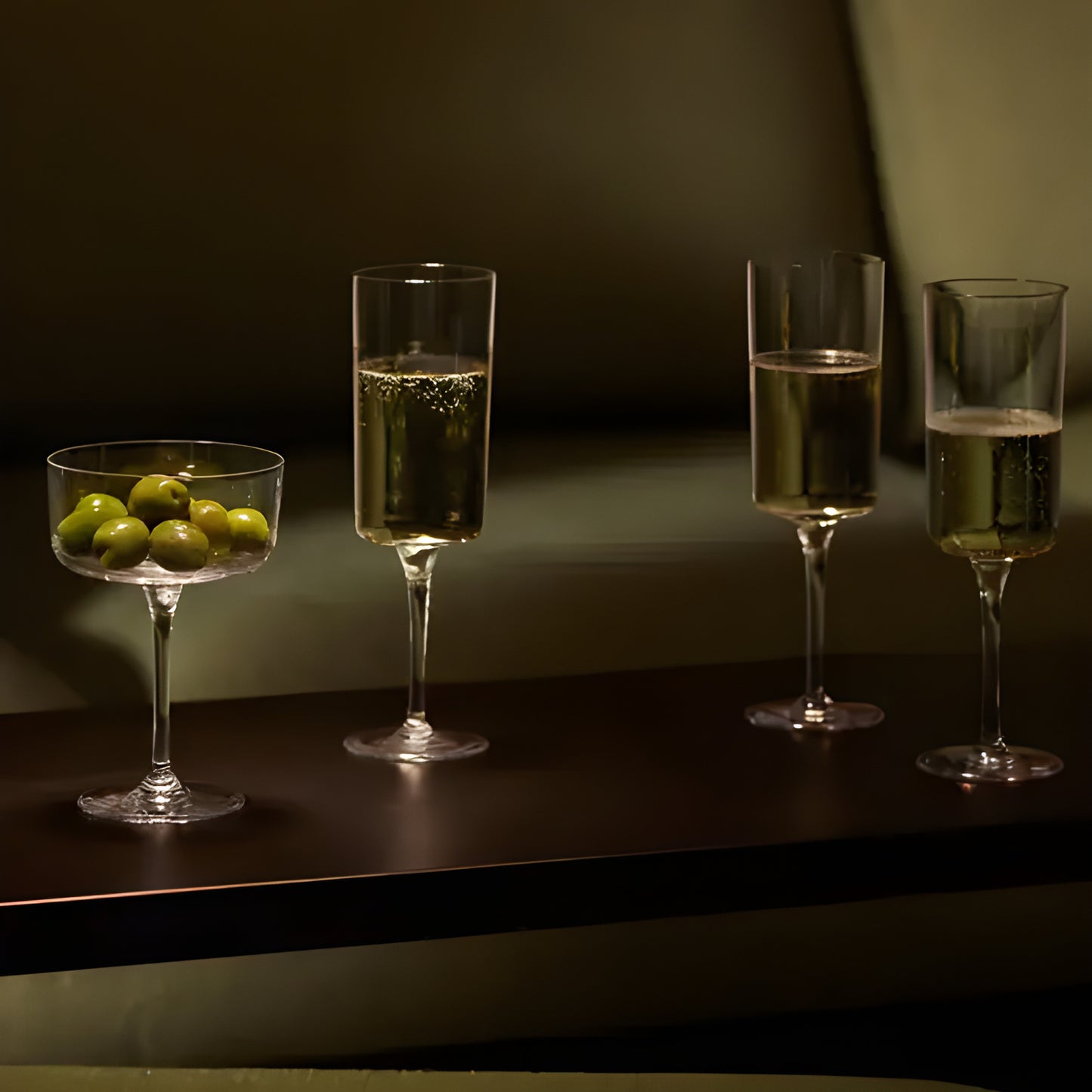 Champagne flutes with sparkling wine and a bowl of olives on a table.