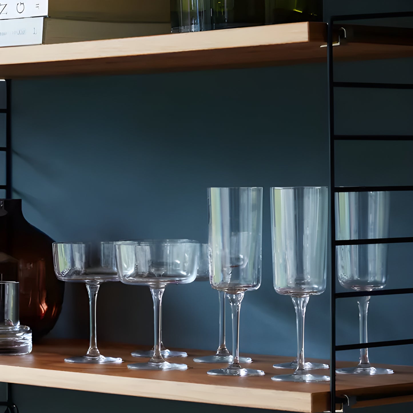 Assorted glassware including champagne flutes on a wooden shelf.