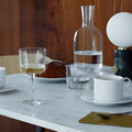 Modern dining table with wine glass, marble top, and water carafe.
