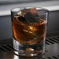 A glass of whiskey with a large ice cube on a modern bar counter.