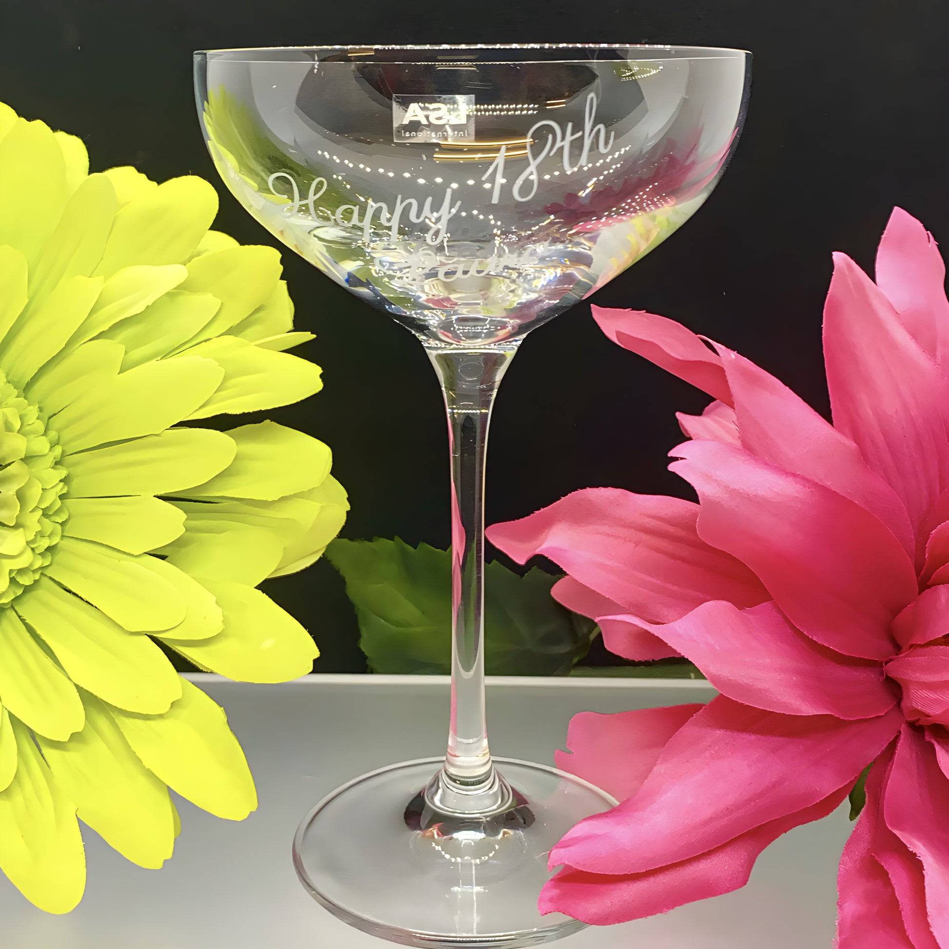 Engraved champagne saucer with 'Happy 18th Birthday' surrounded by yellow and pink flowers.