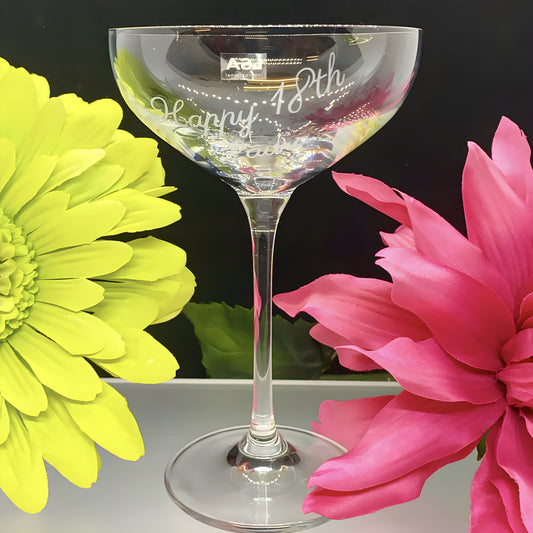 Engraved champagne saucer with 'Happy 18th Birthday' surrounded by yellow and pink flowers.