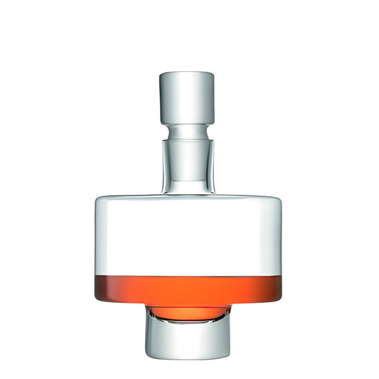 Modern glass decanter with stopper holding red liquid against white background.