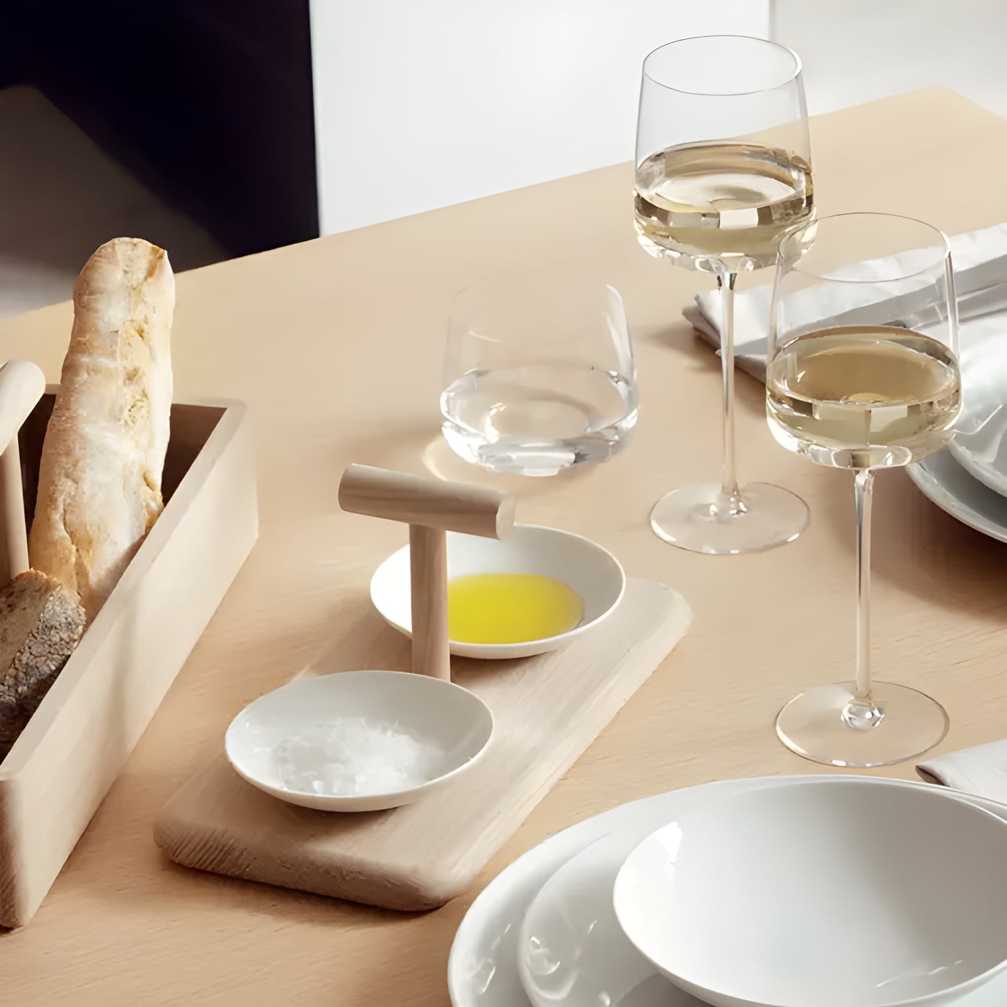 Elegant dining table with wine glasses, bread, and white plates.