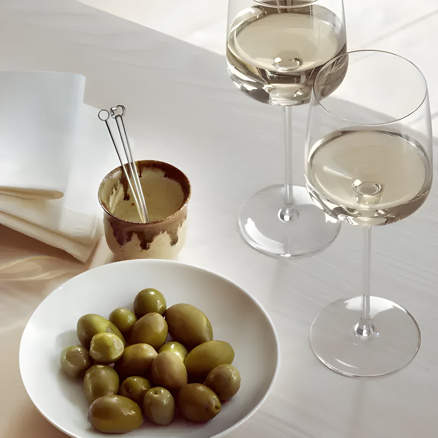 Two wine glasses with white wine and olives on a table.