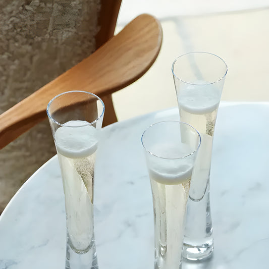 Three tall champagne flutes on a marble table with wooden chair in background.