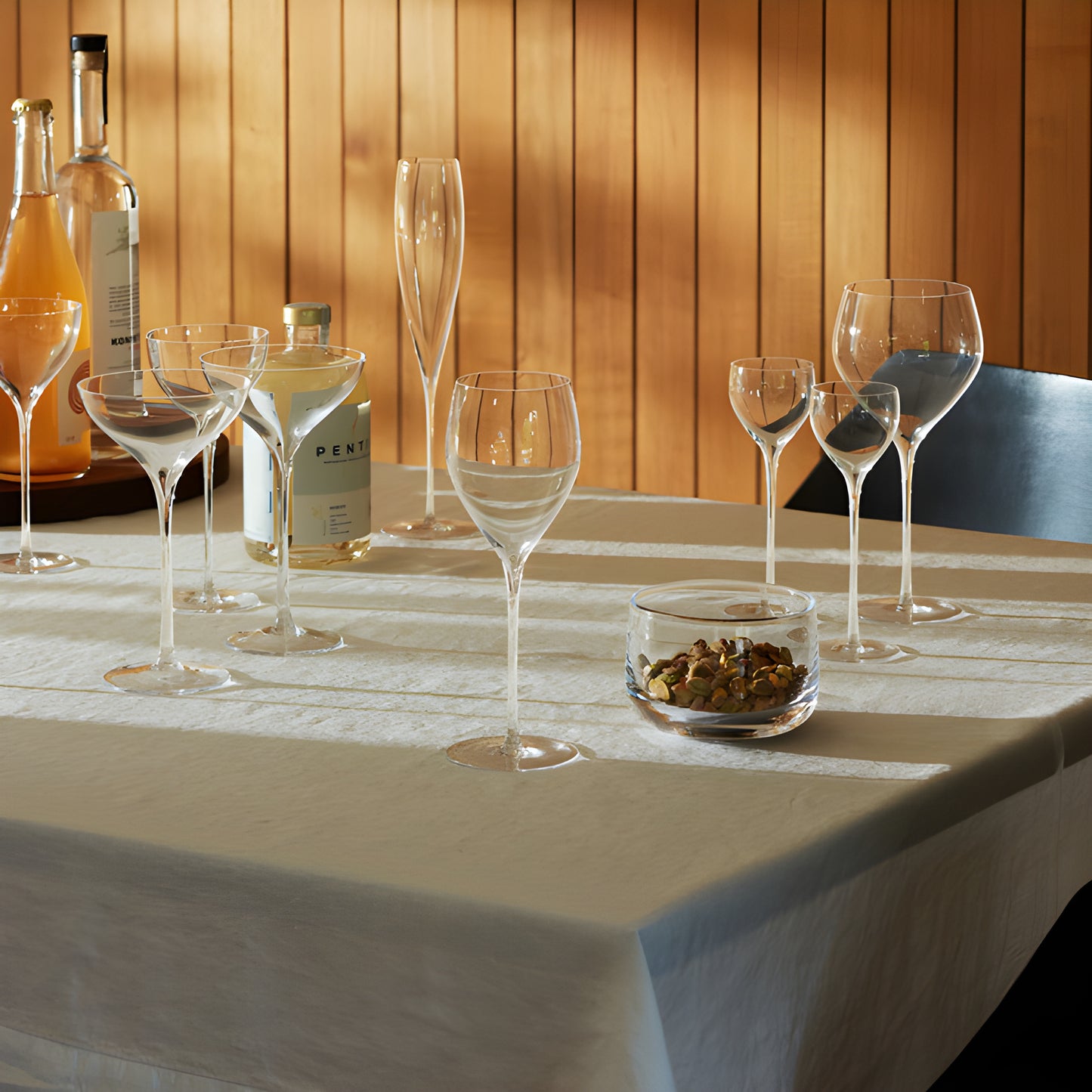 Elegant table setting with various glassware and bottles under warm lighting.
