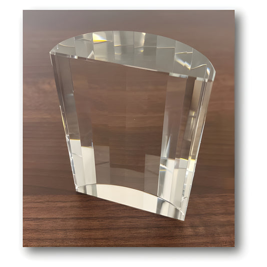 Clear glass award with scalloped back on wooden table, reflecting light