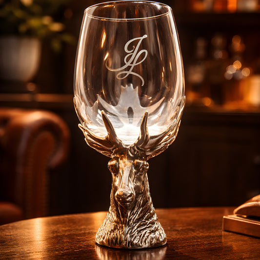 Decorative wine glass with stag head base on wooden table.
