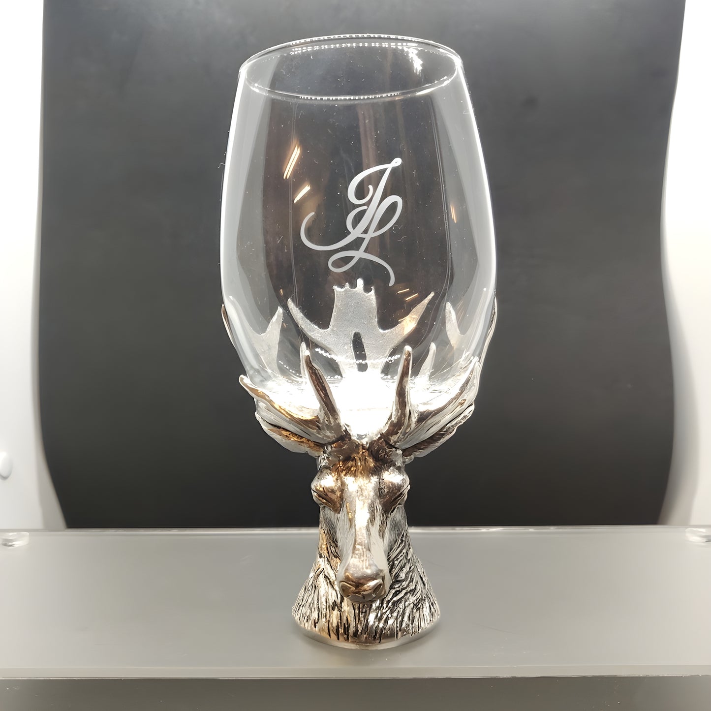 Wine glass with stag head base and engraved initials on a dark background.