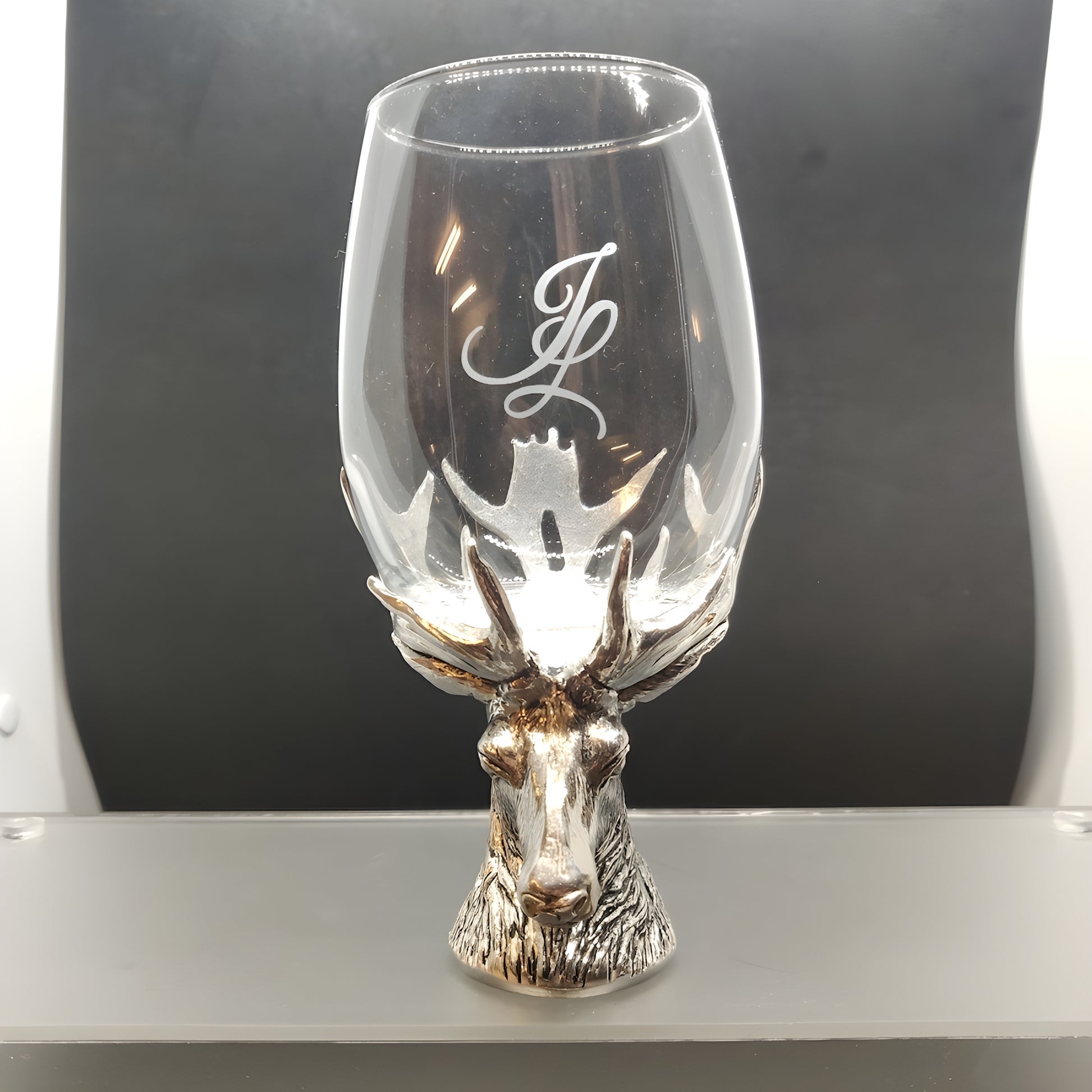 Wine glass with stag head base and engraved initials on a dark background.
