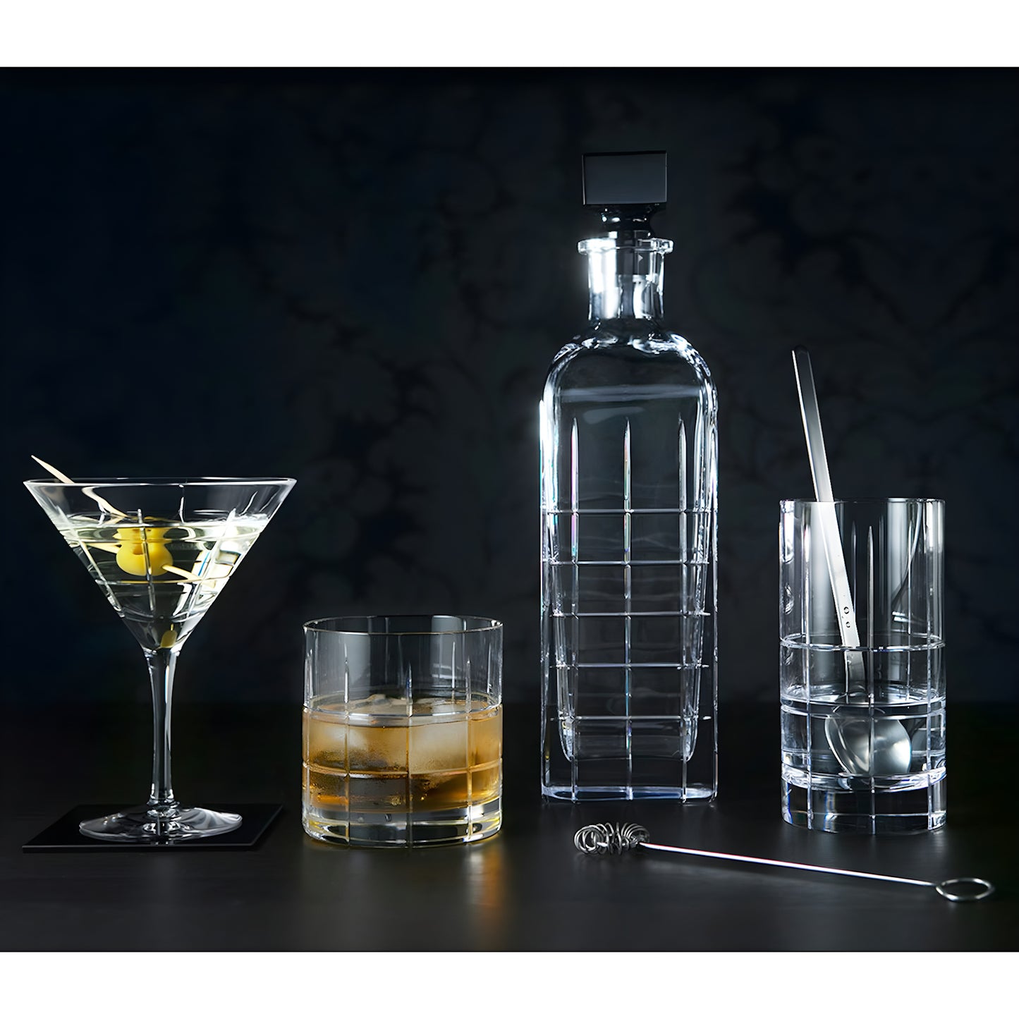 Elegant glassware set with decanter, martini, cocktail, and highball glasses on a dark background.