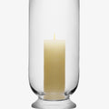 Glass hurricane candle holder with a lit white pillar candle.